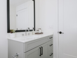 2-BR Apartments in Arlington, VA - Sage at National Landing - Bathroom with White Countertop, Grey Cabinets, Tile Flooring, a Large Mirror, and Stylish Decor