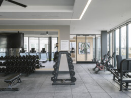 Studio Apartments in Arlington, VA - Sage at National Landing - Fitness Center with Cardio Machines, Free Weights, Mirrors, a Ceiling Fan, and Large Windows