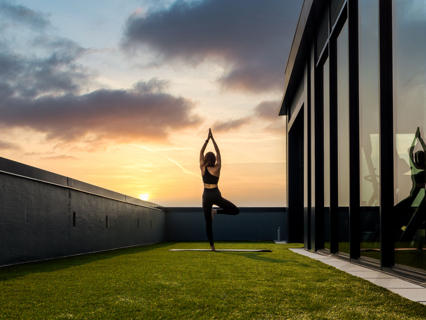1-BR Apartments in Arlington, VA - Sage at National Landing - Outdoor Part of the Fitness Center with Grass, a Girl on a Yoga Mat, and Beautiful Views